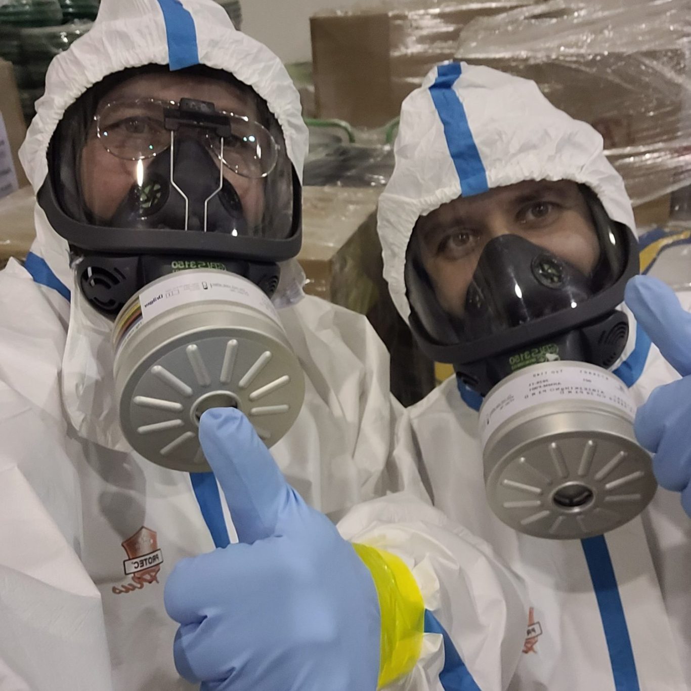 Zwei Fachkräfte Zwei Fachkräfte in weißen Schutzanzügen mit Atemschutzmasken und Schutzbrillen bei der Vorbereitung professioneller Desinfektionsarbeiten.